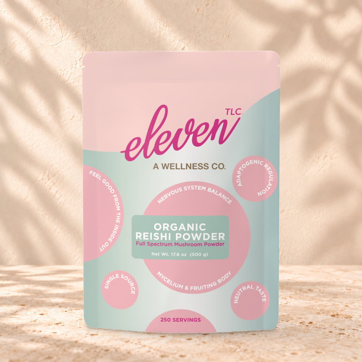 Eleven TLC Organic Reishi Mushroom Powder 500g stand-up pouch on travertine stone against a warm cream plaster wall, lit from the left with a soft shadow to the right.