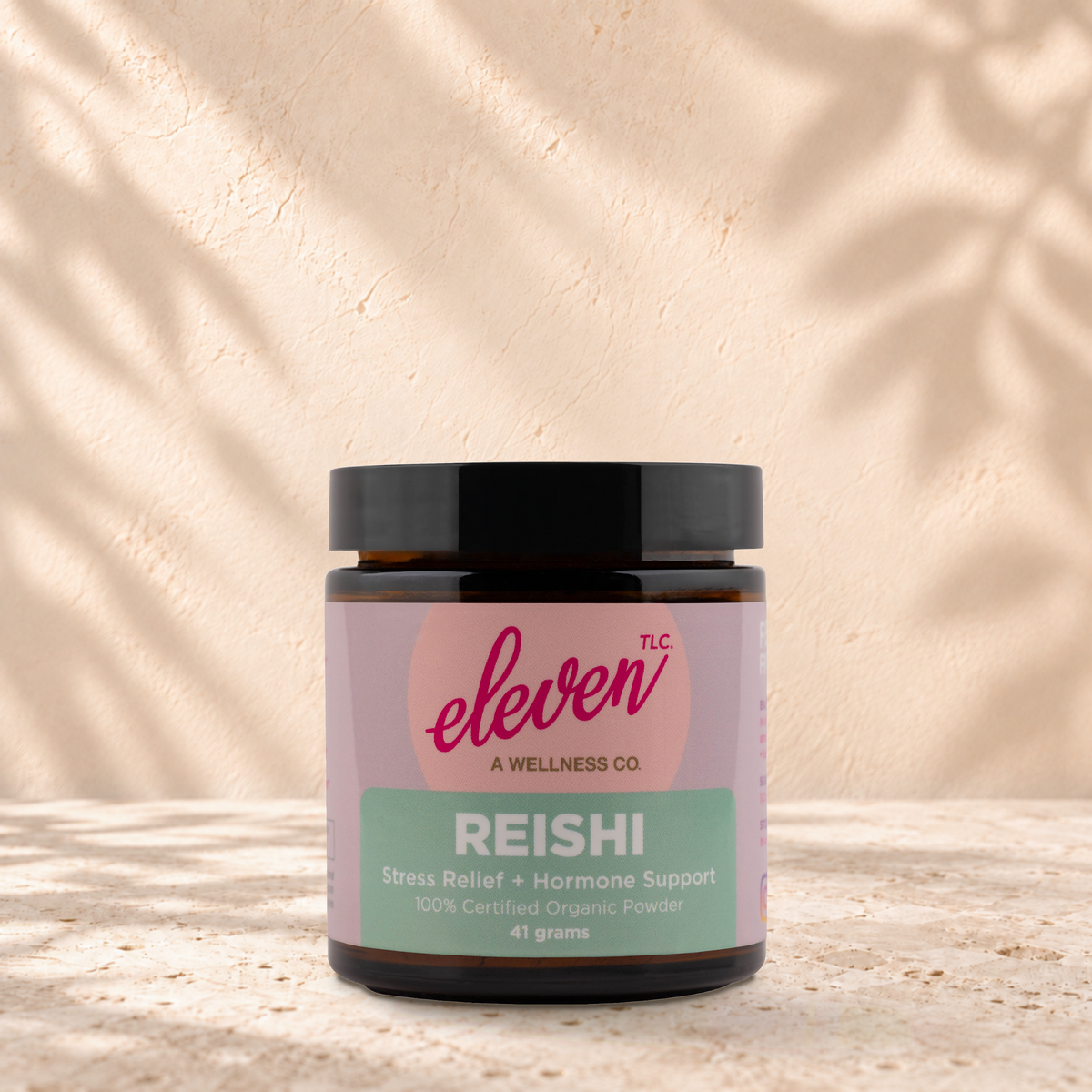 Eleven TLC Reishi 41 gram mushroom powder jar with a black lid standing on travertine against a warm plaster backdrop.