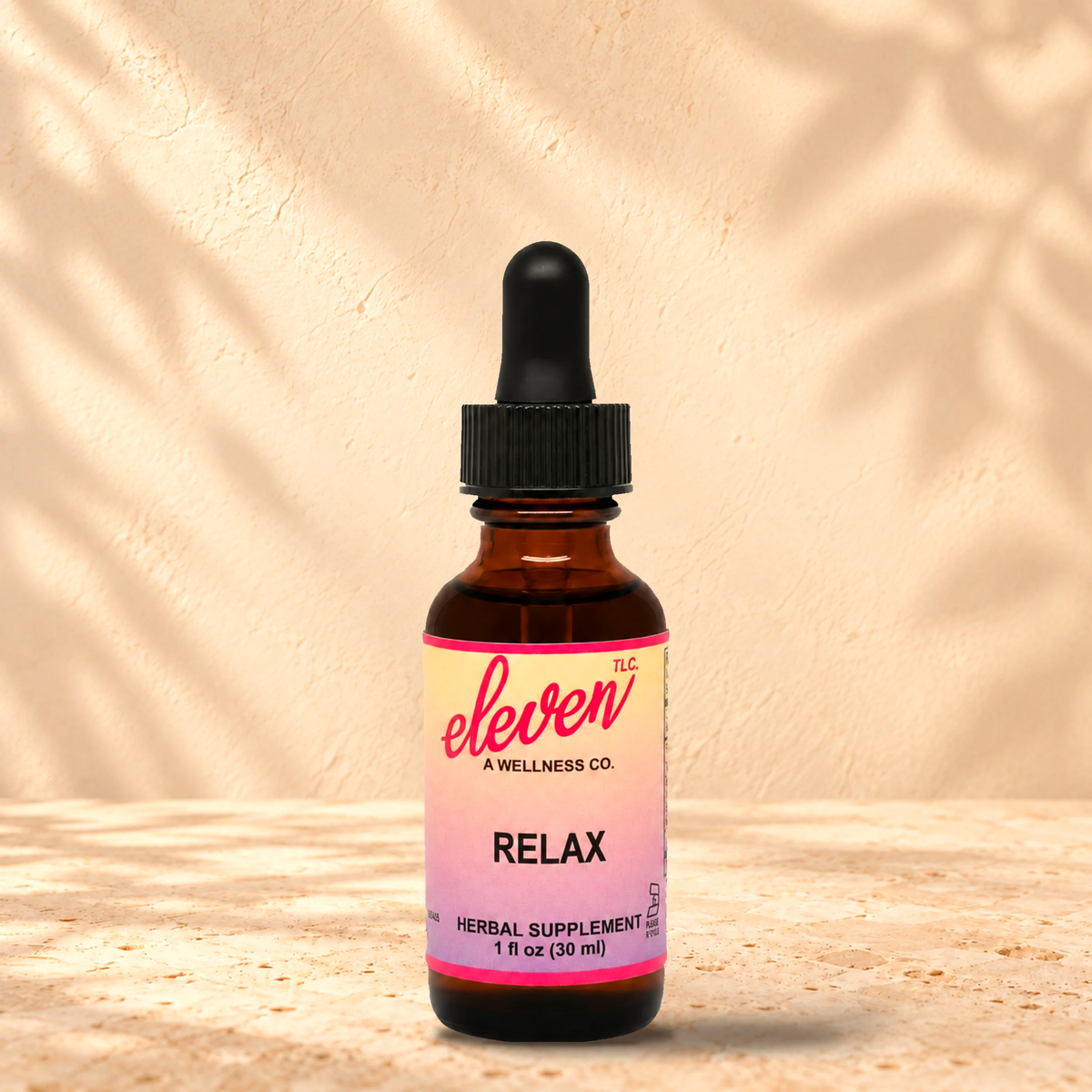Eleven TLC Relax herbal supplement tincture in a 1 fl oz (30 ml) amber glass dropper bottle with a pink-to-lavender label, standing on a stone surface with soft leaf shadows