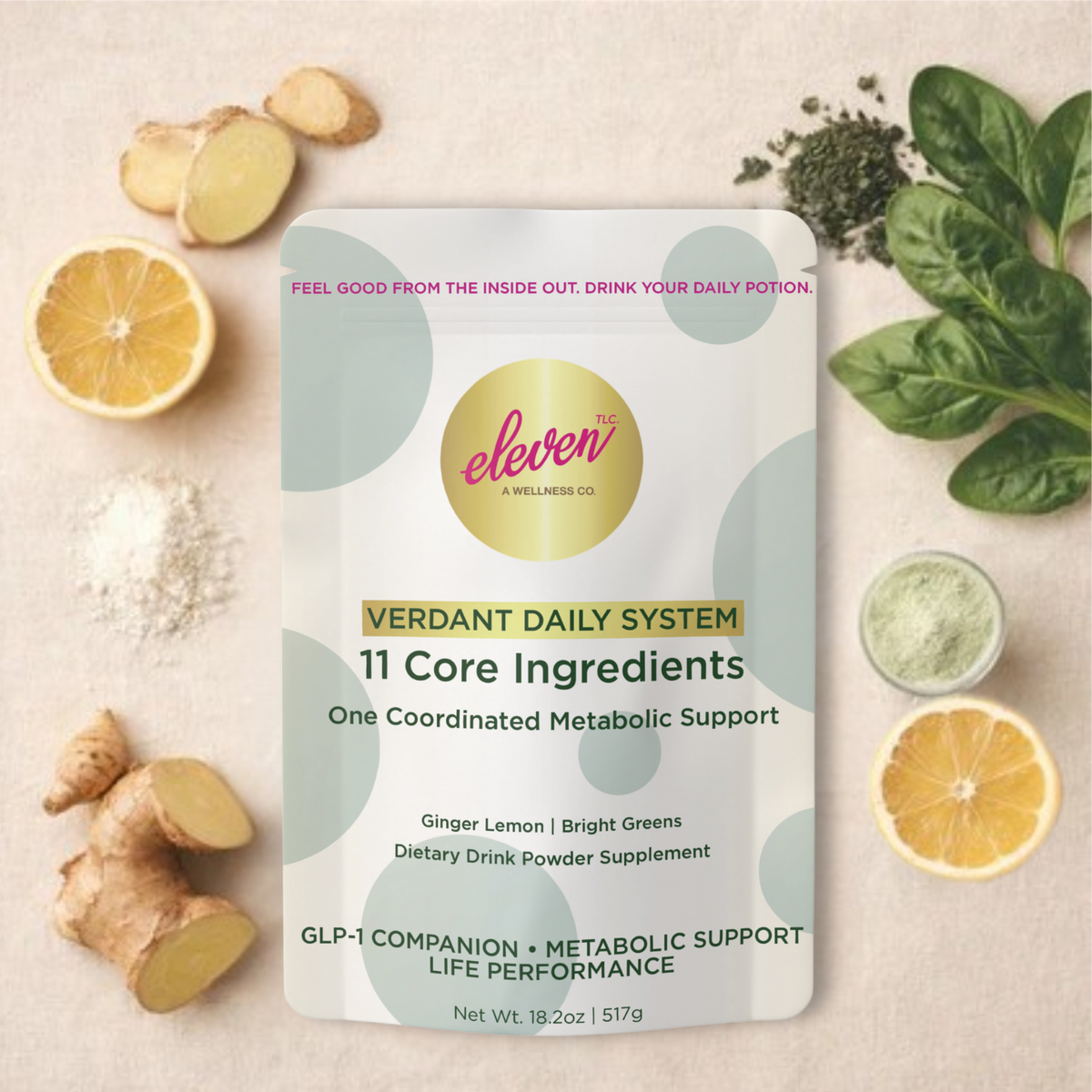 Eleven TLC Verdant Daily System 517g pouch on a cream surface surrounded by lemon halves, sliced ginger, green leaves and bowls of powder.