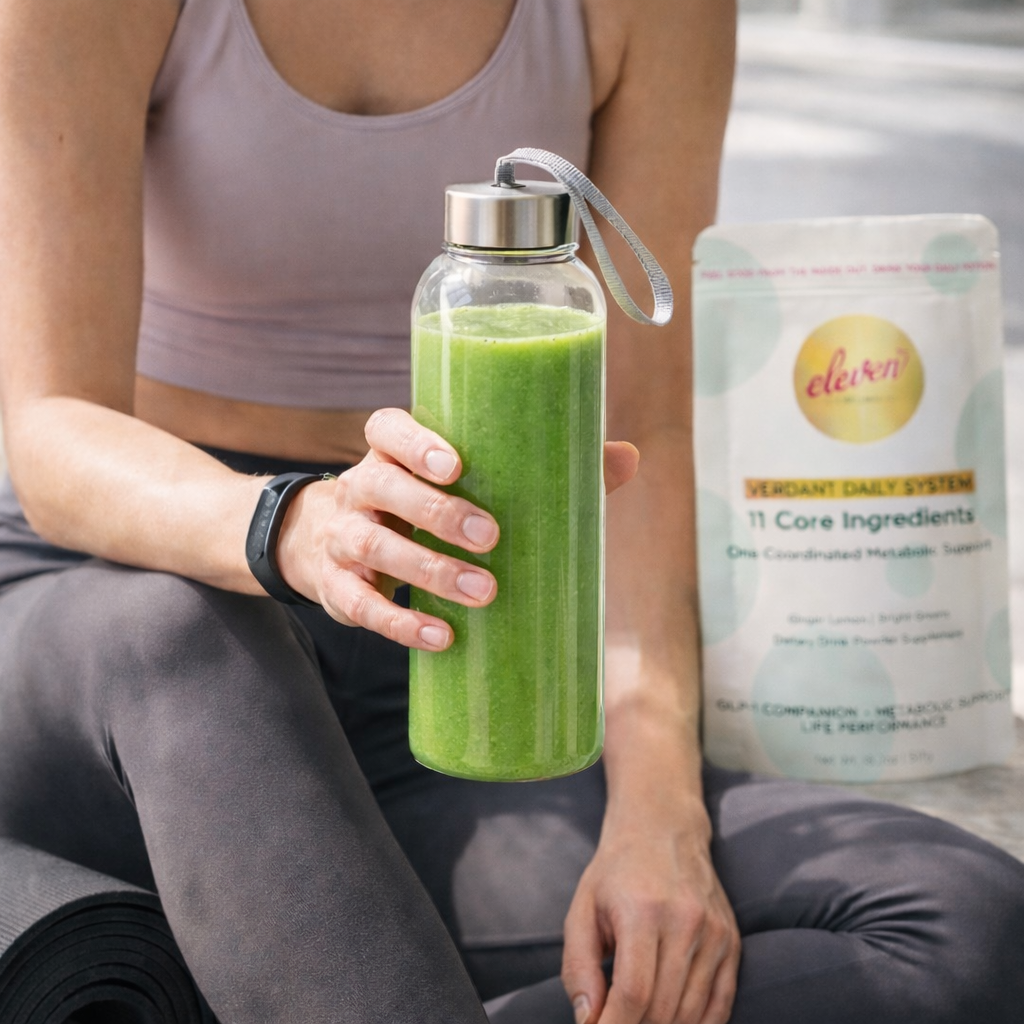 Person holding a glass bottle of green Verdant Daily System beverage with the 517g product pouch on a clean, light-toned surface.
